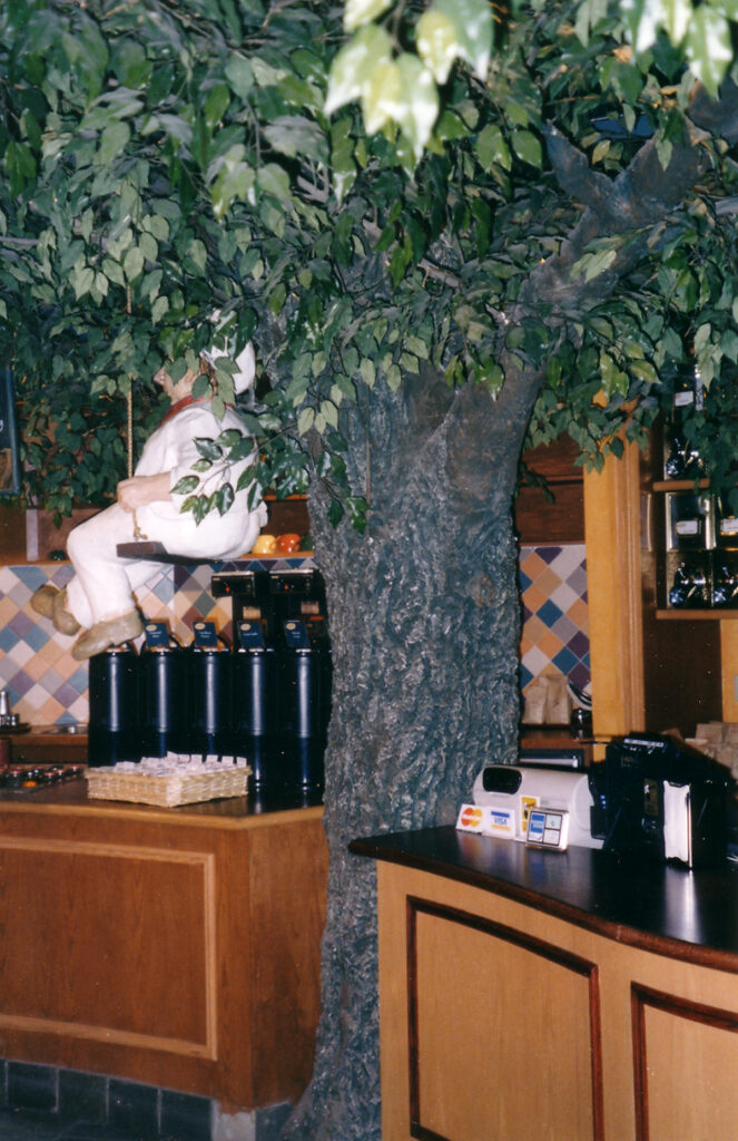 Papier-mâché baker figure positioned among the branches of the Nova Era Bakery tree sculpture